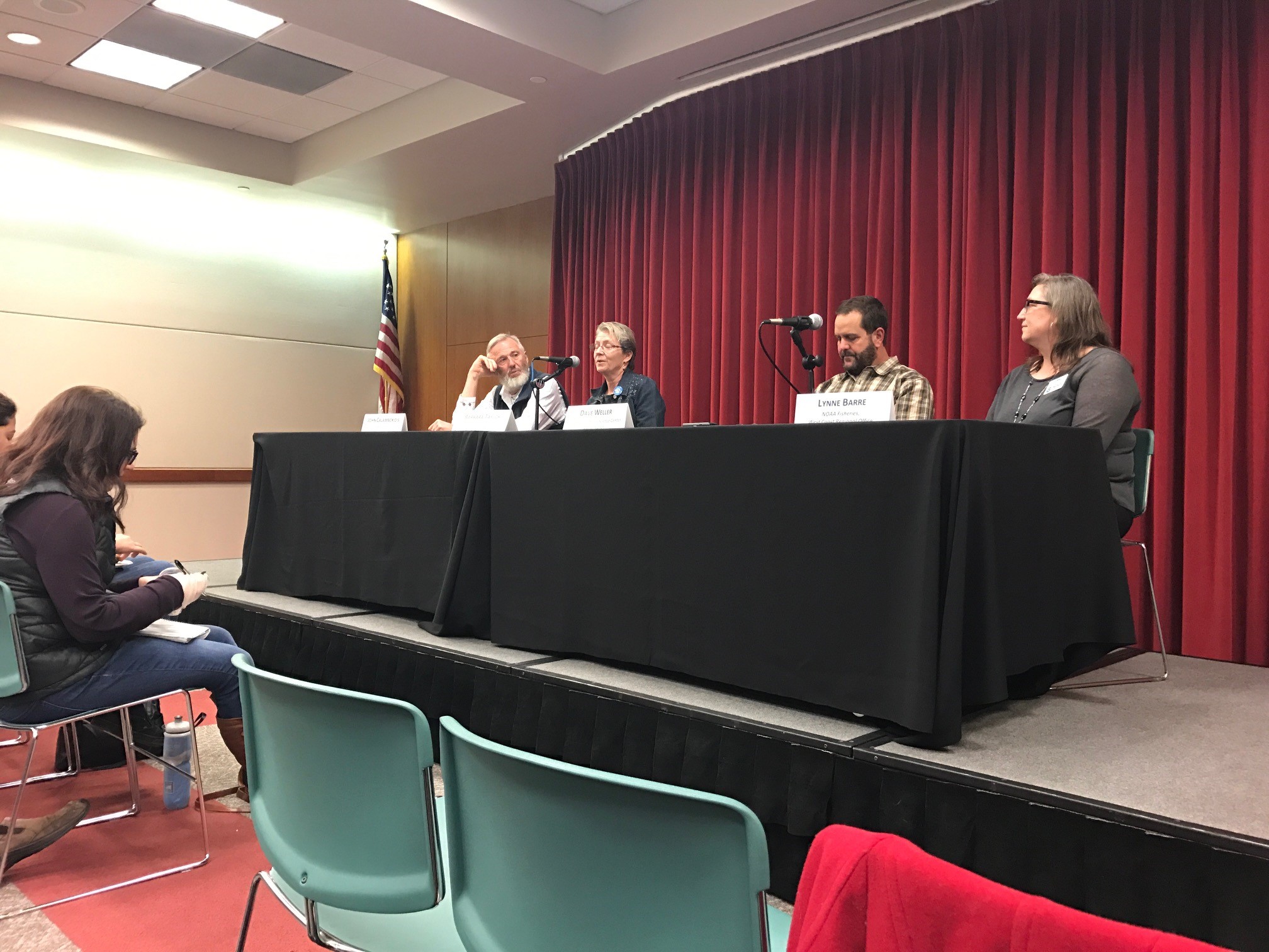 Four people sit at table on stage while people sit in audience