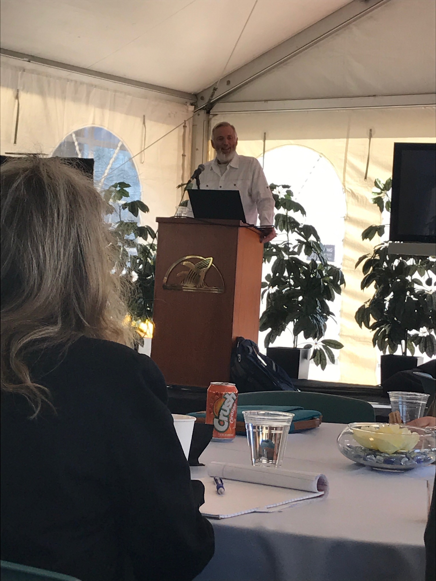 person stands at podium with a computer under a canopy