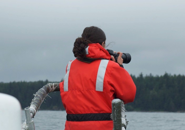 the back of a person on a boat in a neon orange coat with a camera